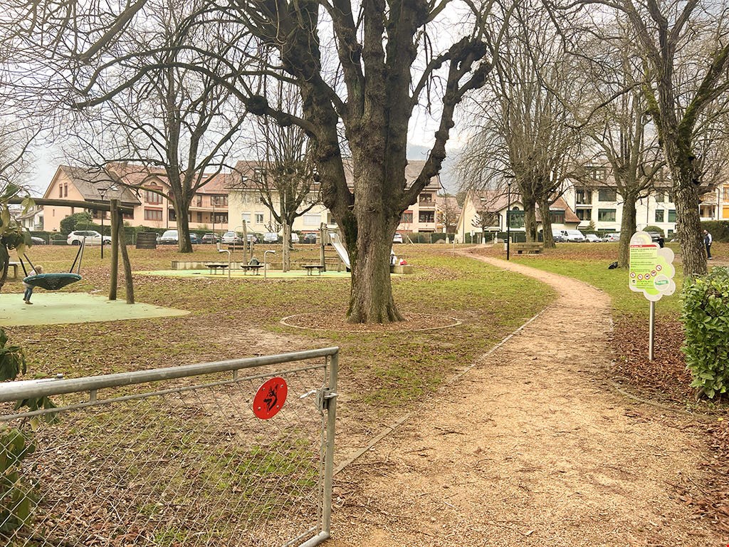 Park with gravel pathway, playground, trees, and residential buildings in the background