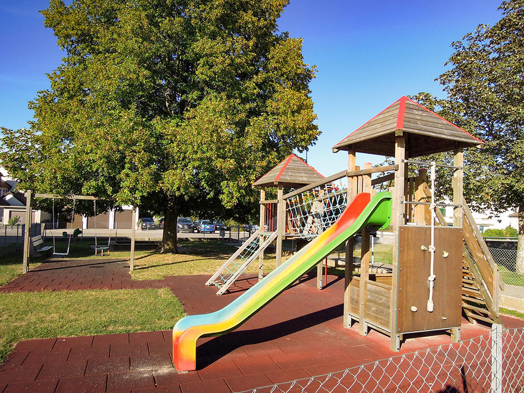 a slide, a climbing frame, and swings in a fenced outdoor area