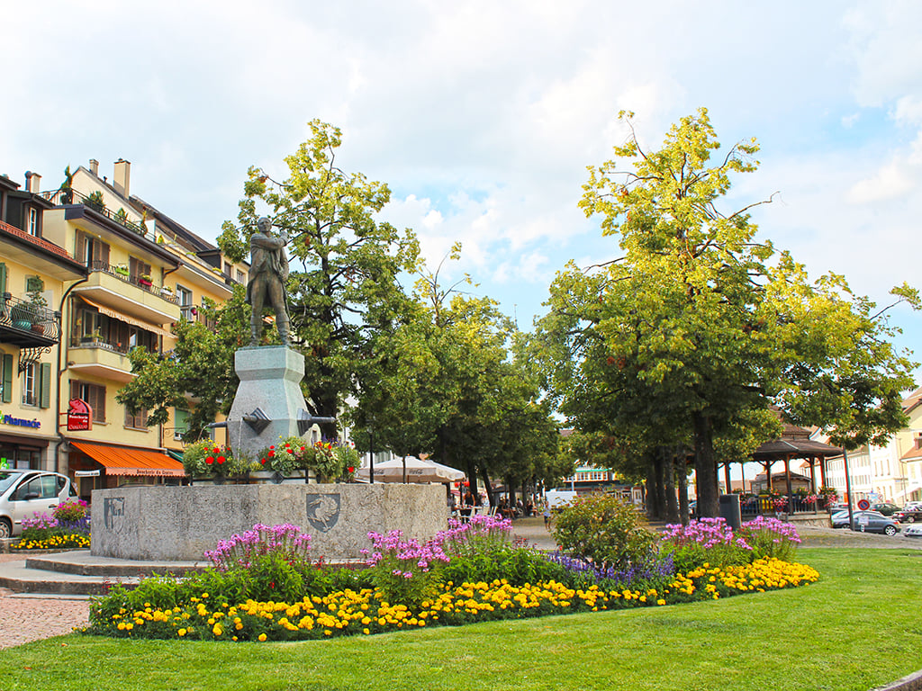statue, flowers, trees, buildings, parking lot