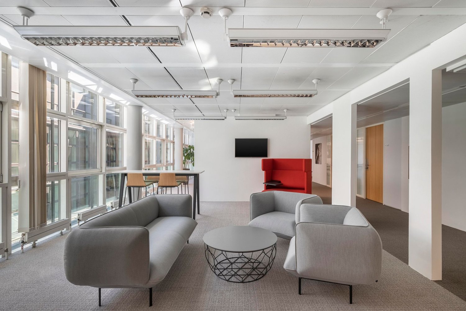modern office room with gray couches, round table, TV, large windows, wooden door