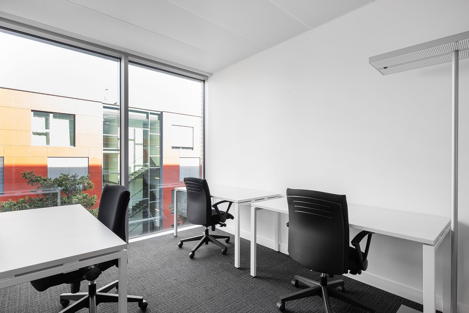 Bright and modern office space with large windows providing a view, white walls, black office chairs, and white desks.