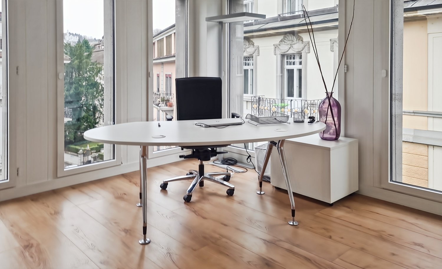 an office room with a round desk, a black chair, glass windows, and a glass door