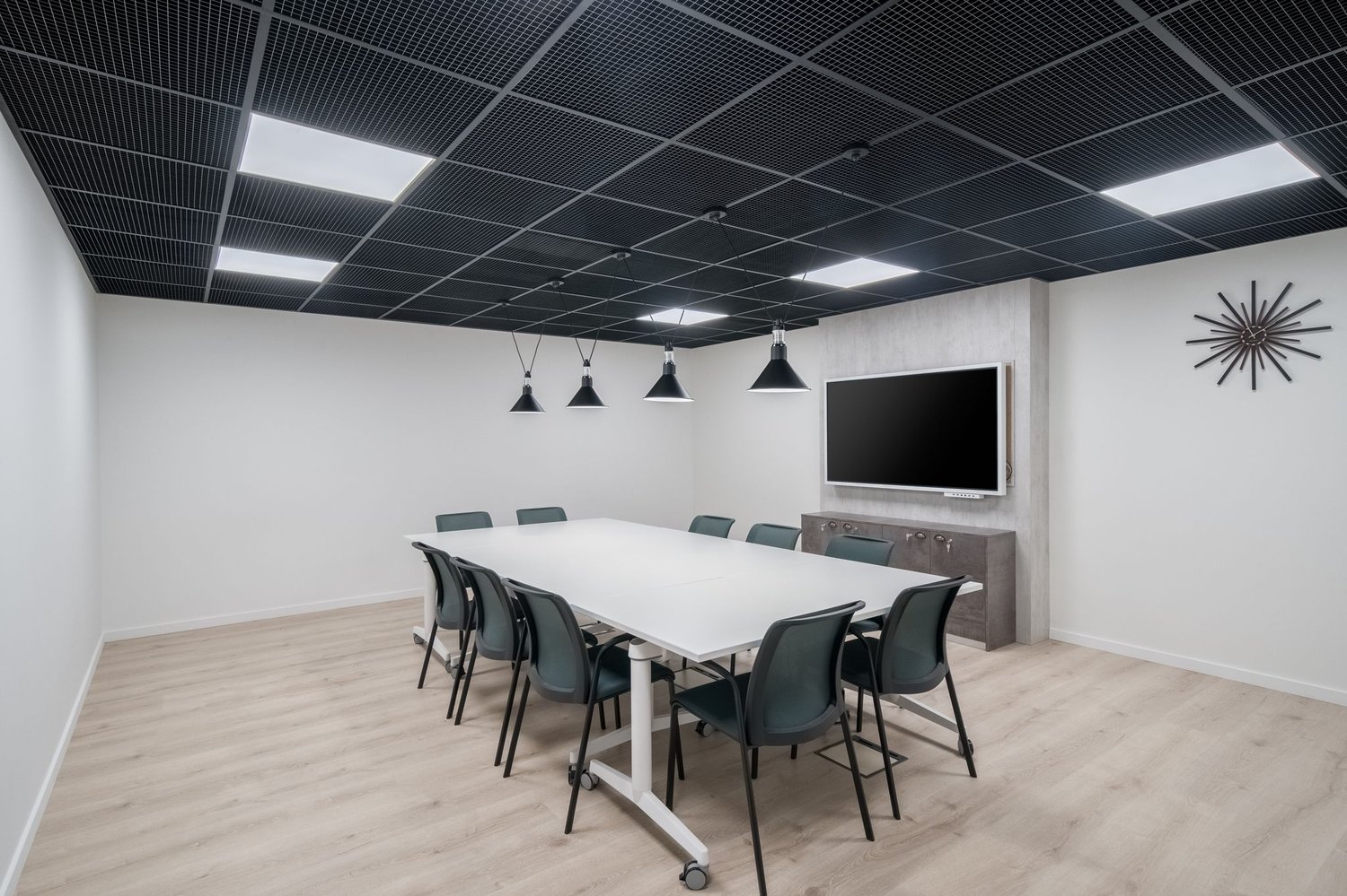 modern meeting room with a long white table, black chairs, a flat screen TV, and a gray cabinet