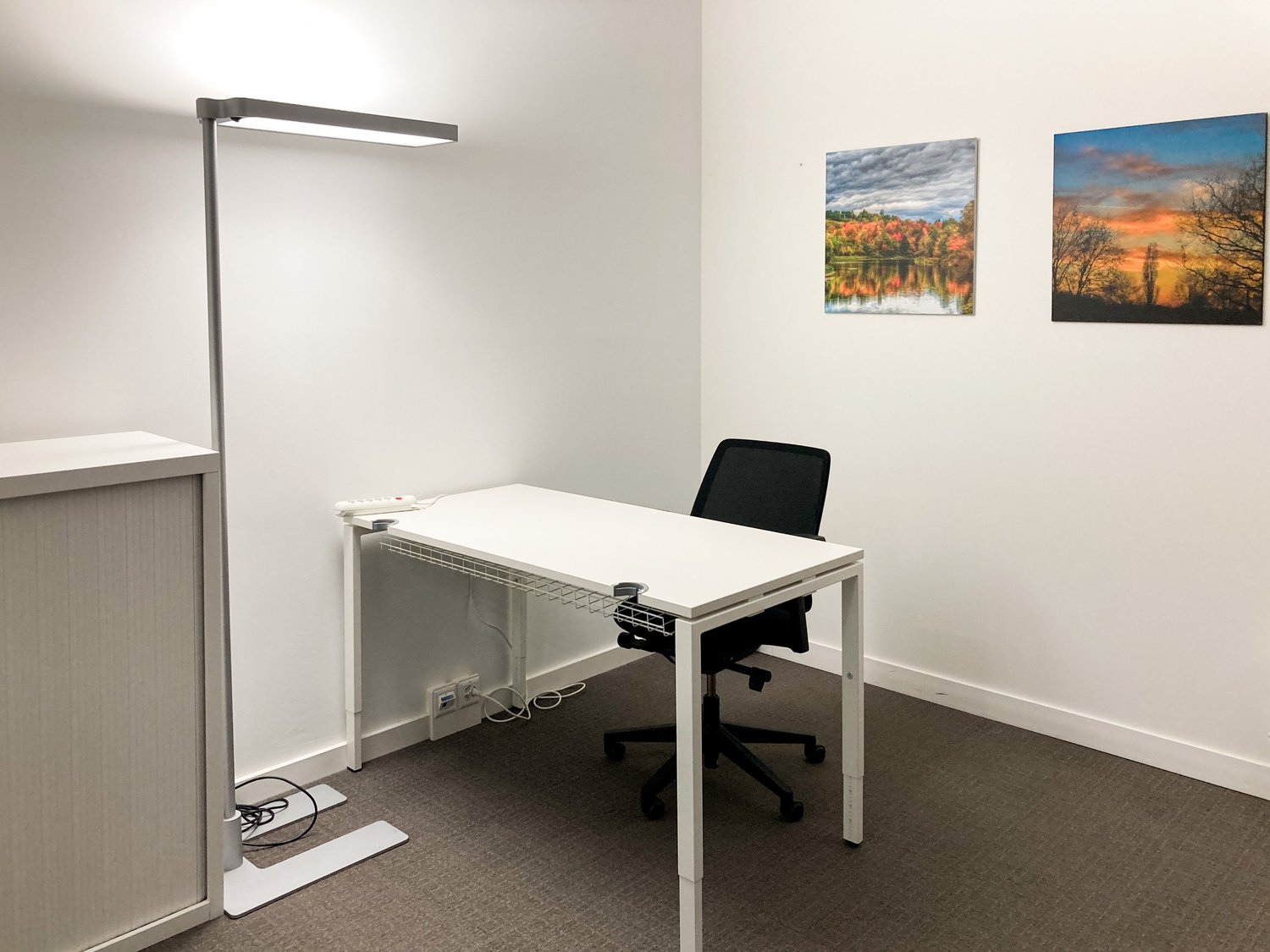 small office with a desk, a chair, a lamp, and two paintings on the wall