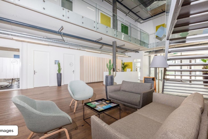 modern open office space, glass staircase, reception area, light wood floor, gray sofa, coffee table, potted plants, glass railings, chalkboard sign