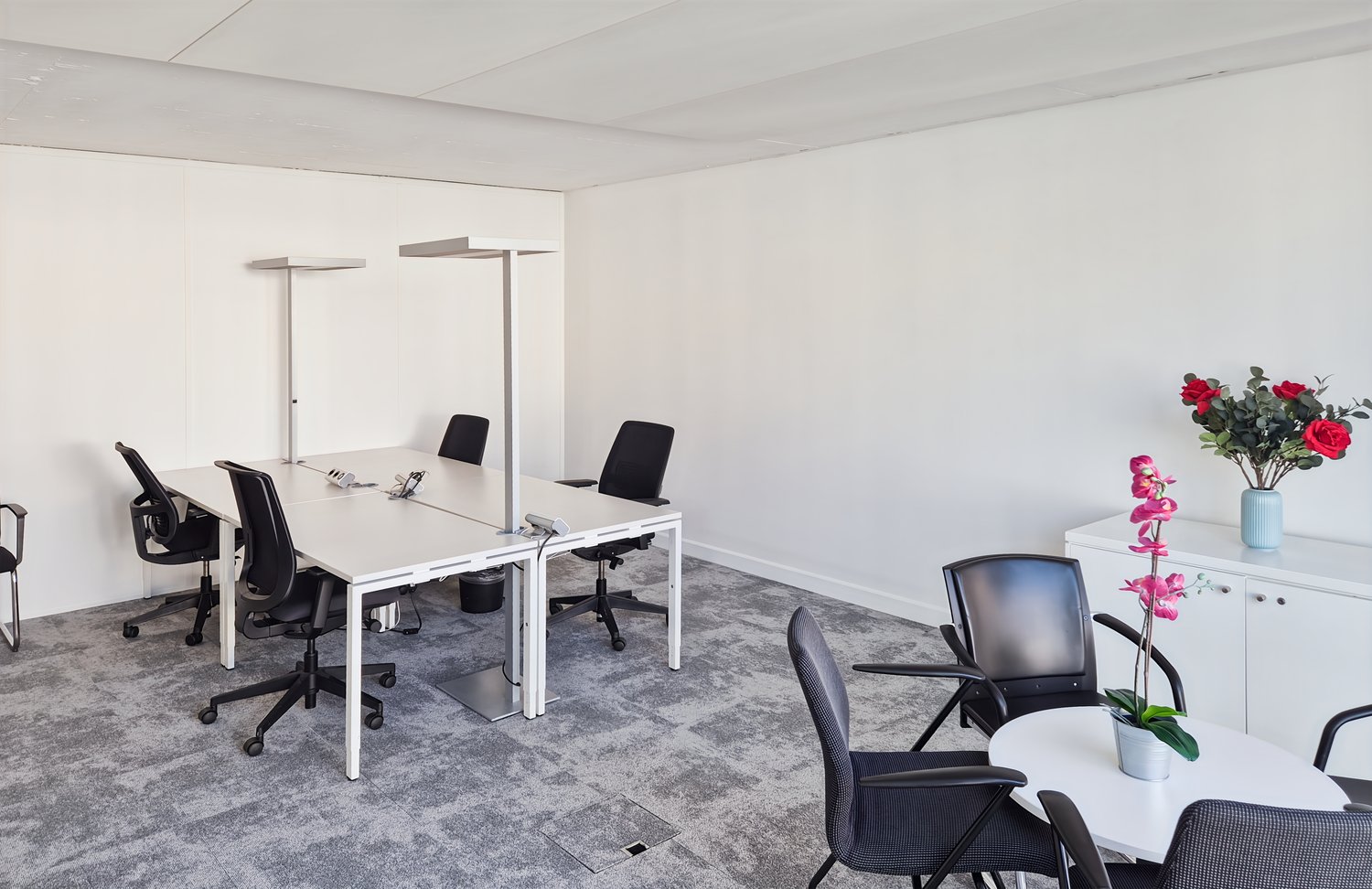 modern office room with white walls, gray carpet, white desks, black chairs, white cabinets, flowers