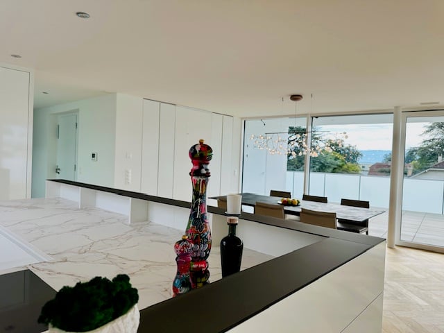 Open plan kitchen, dining and living room with large windows, glass doors to the terrace, modern appliances, black countertop, marble flooring, modern art