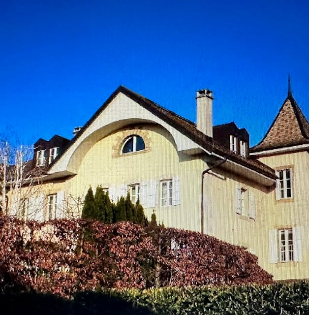 large yellow house with a brown roof, multiple windows, small trees and shrubs