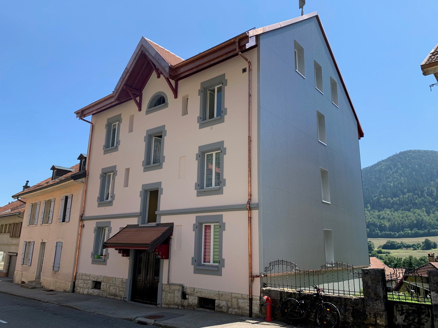 Raised ground floor house, multiple windows, brown roof, stone facade, gated entrance, bicycles parked