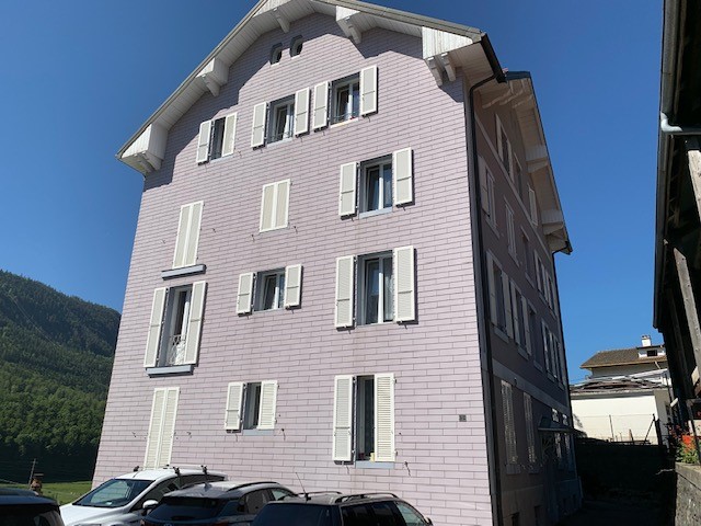 3 story building, pink brick, white windows, parking area in front