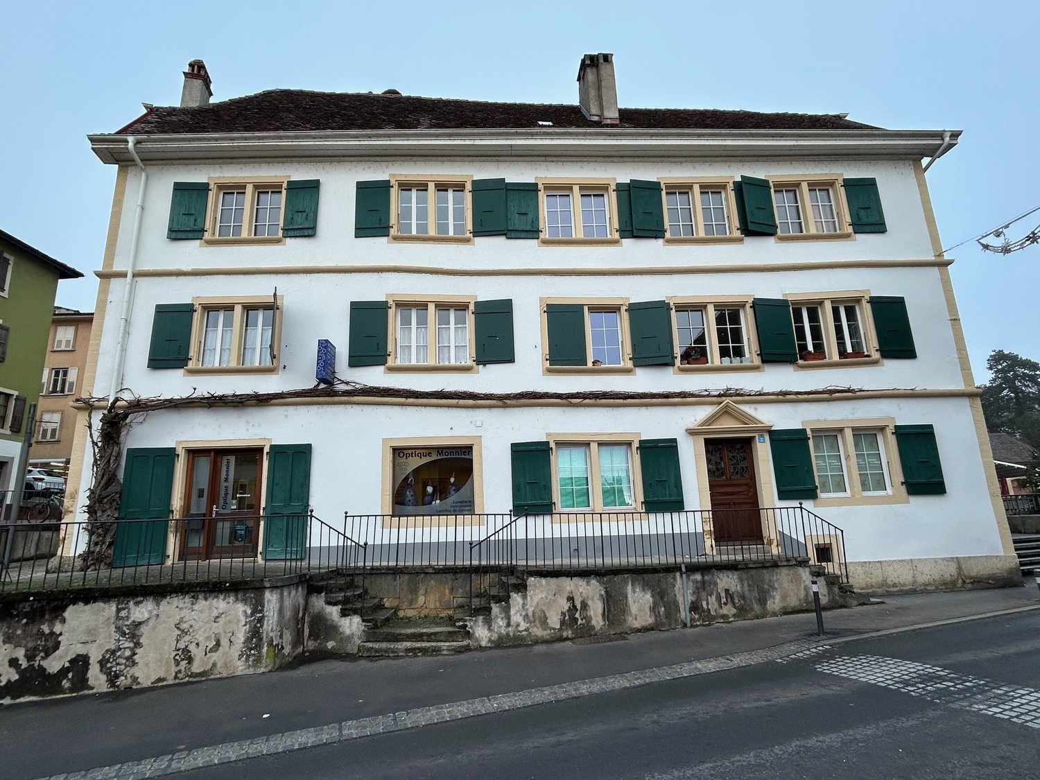 3-story house, white painted, green shutters, large windows, steps at entrance, brown door, metal railings