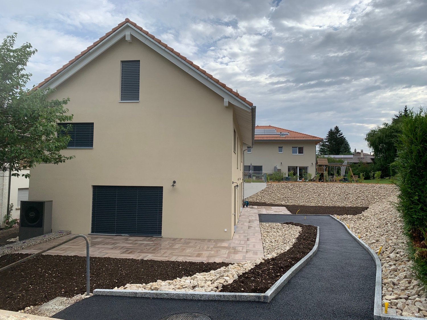Modern 2 story house, beige, with garage, concrete driveway, gravel path, solar panels on the back house.