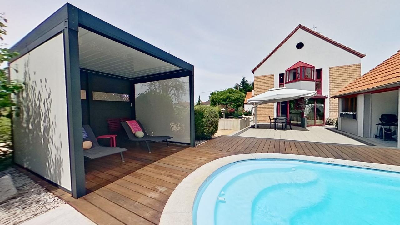 Two-story house with a modern design, featuring a swimming pool, a covered patio or balcony area, and a wooden deck surrounding the pool.