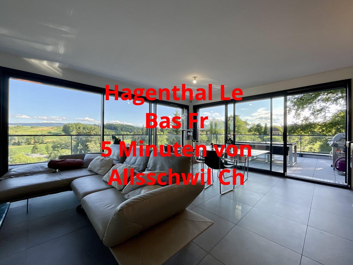 Spacious living room with large windows offering a scenic view of the surrounding landscape, modern furniture including a sectional sofa, and a tiled floor.