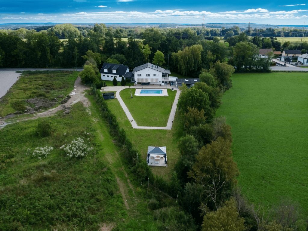 Large villa with modern architecture, large pool, surrounded by lush greenery, spacious yard, distant buildings, clear sky