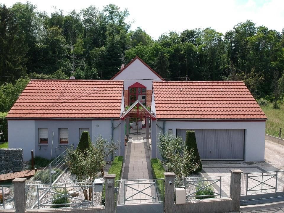 White house with red roof, garage, garden with trees, gate, and a pathway to the entrance