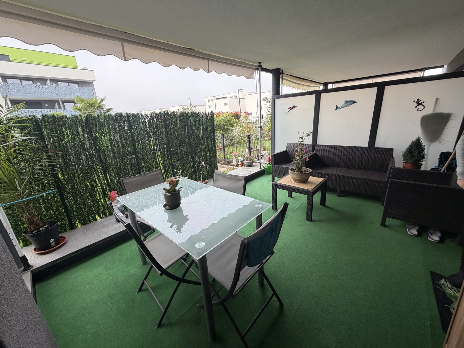 Terrace with green carpet, table and chairs, potted plants, and an awning.
