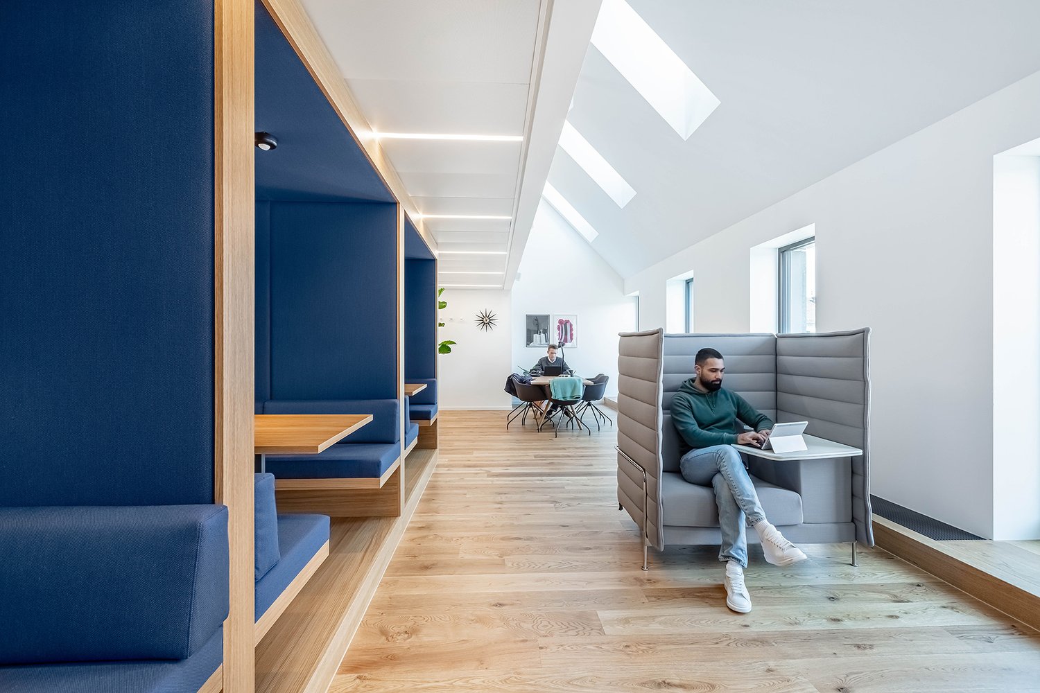 Blue cushioned booths, light wooden flooring, white walls, high ceiling with skylights