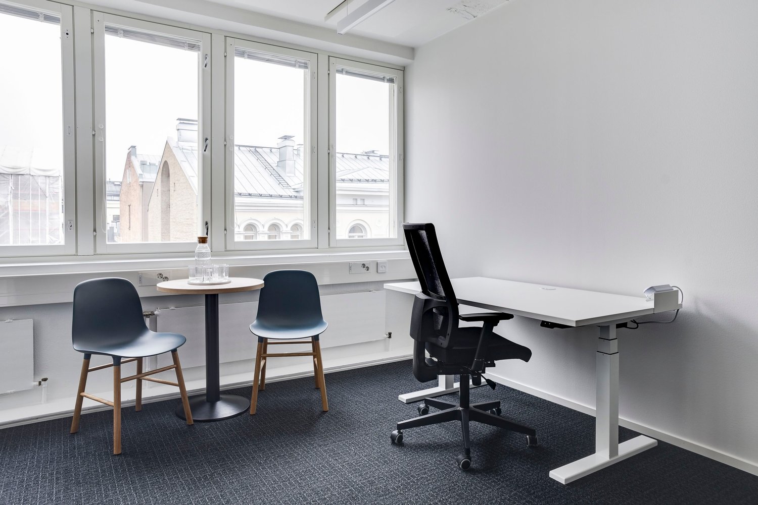 Bright and modern office space with large windows, adjustable desk, chairs, and a small round table