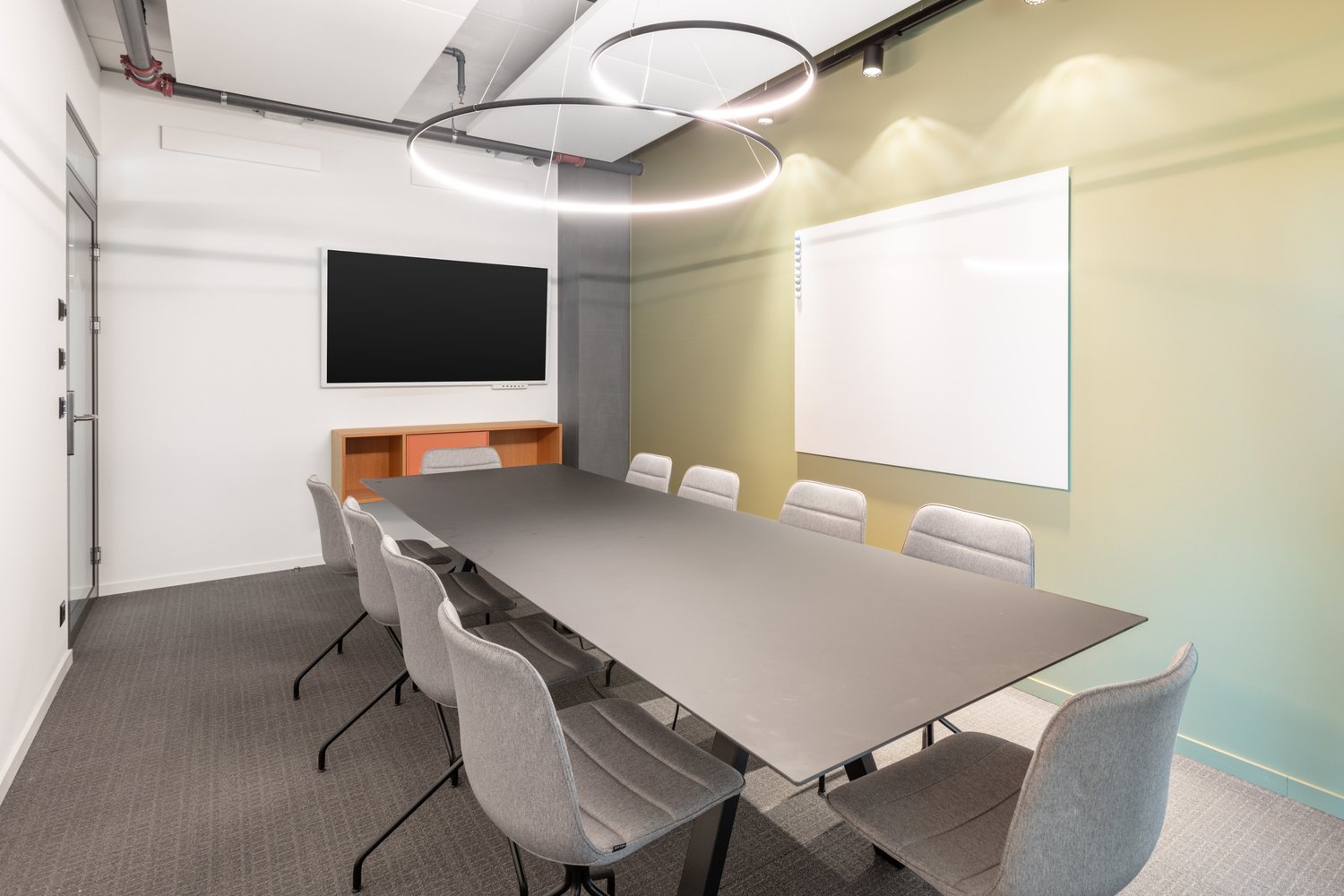 Modern conference room with large table, gray chairs, TV screen, and whiteboard