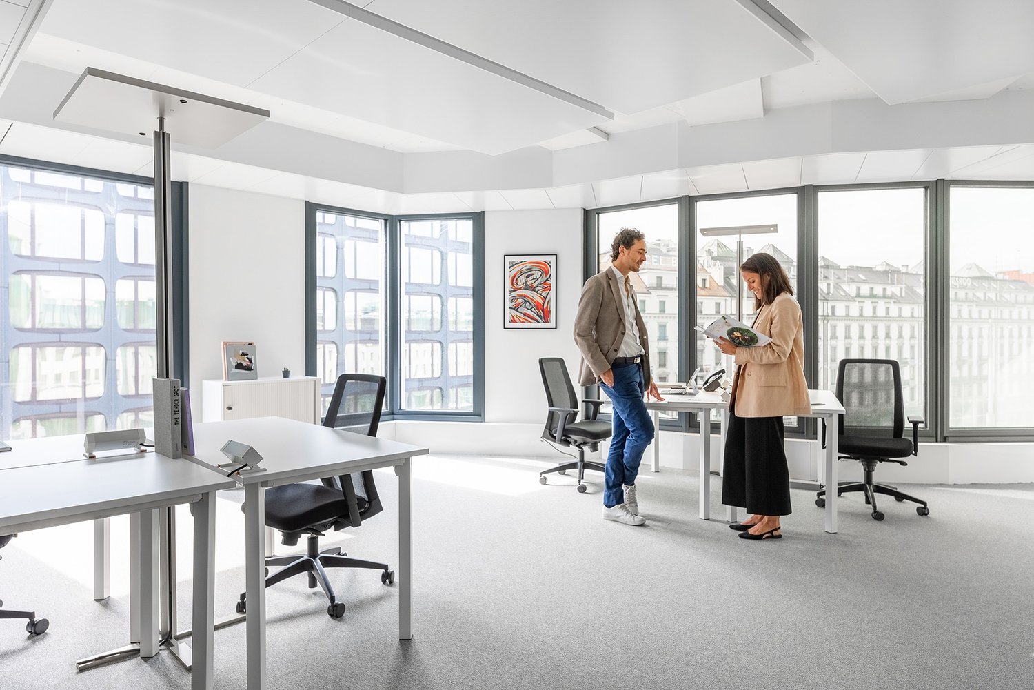 Contemporary office with large windows, a central desk, modern swivel chairs, and decorative elements. View of the cityscape visible through the windows.
