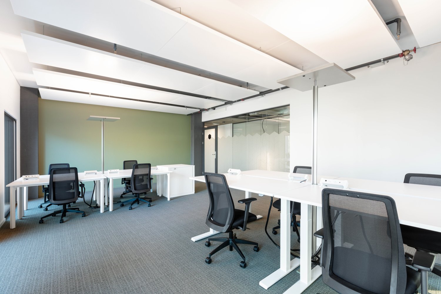 Empty room with white desks and chairs, modern lighting, glass wall