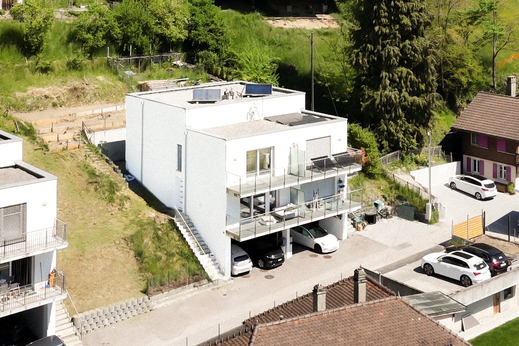 3-story modern white house with balconies, garage, and parking spaces, surrounded by trees and greenery