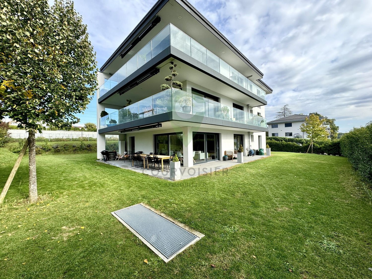Modern two-story house with glass balconies, spacious living area, and garden with outdoor dining setup