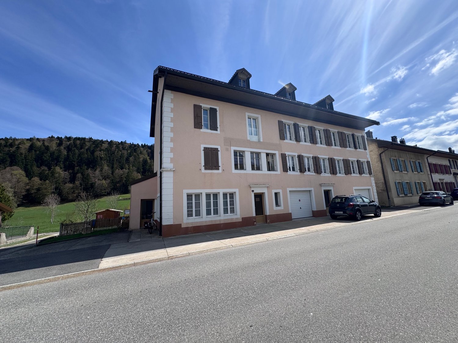 3 story building, beige and brown exterior, multiple windows, 2 garages, 2 cars parked in front