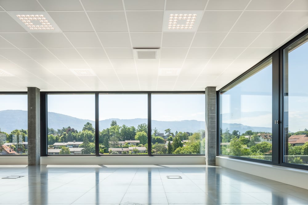 Large open office space with floor-to-ceiling windows offering a panoramic view of the surrounding mountains and greenery. The space features a clean, modern design with a tiled floor, recessed lighting, and a minimalist aesthetic.
