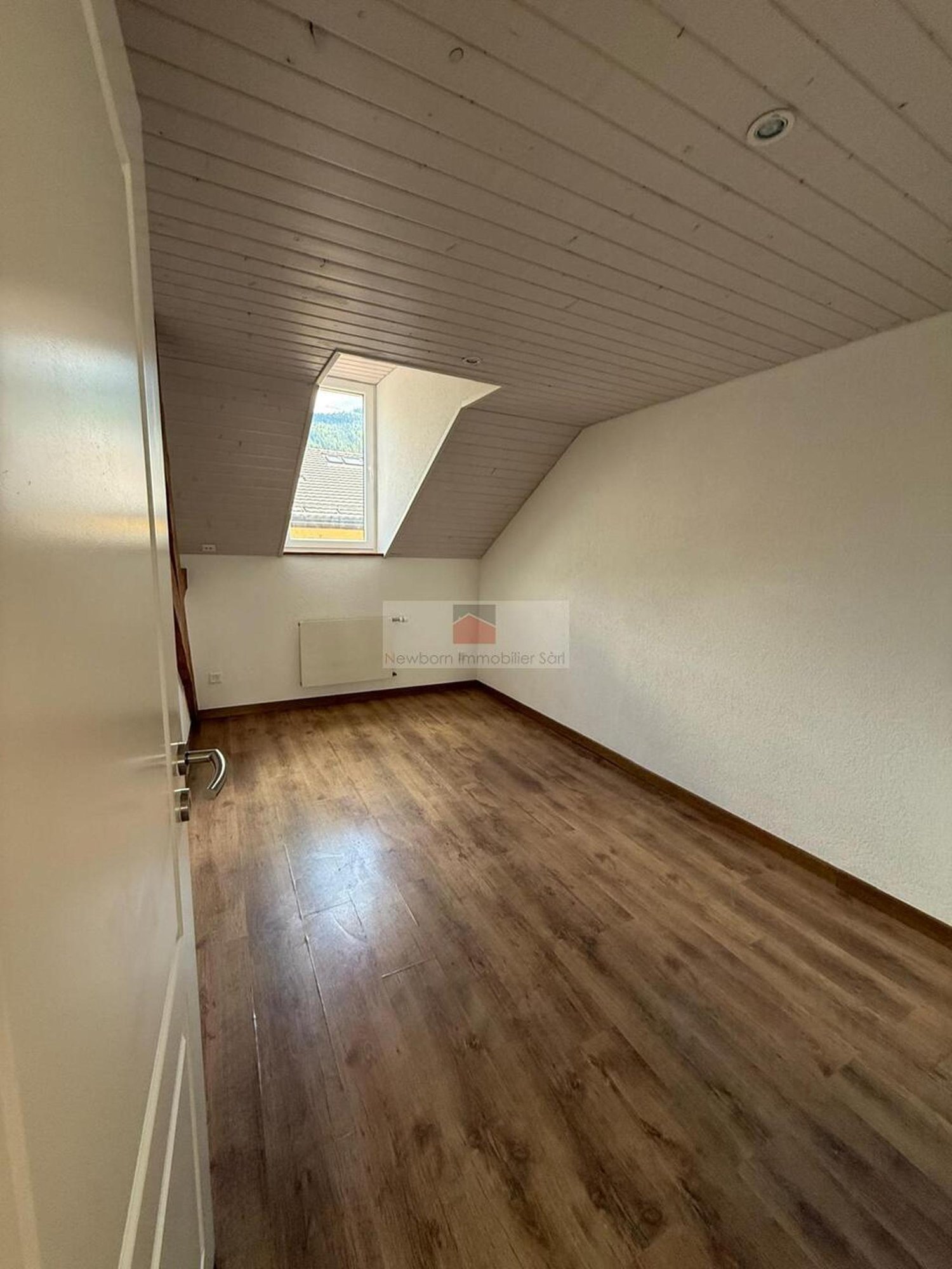 Empty room with wooden floor, white walls, a window, and a ceiling light