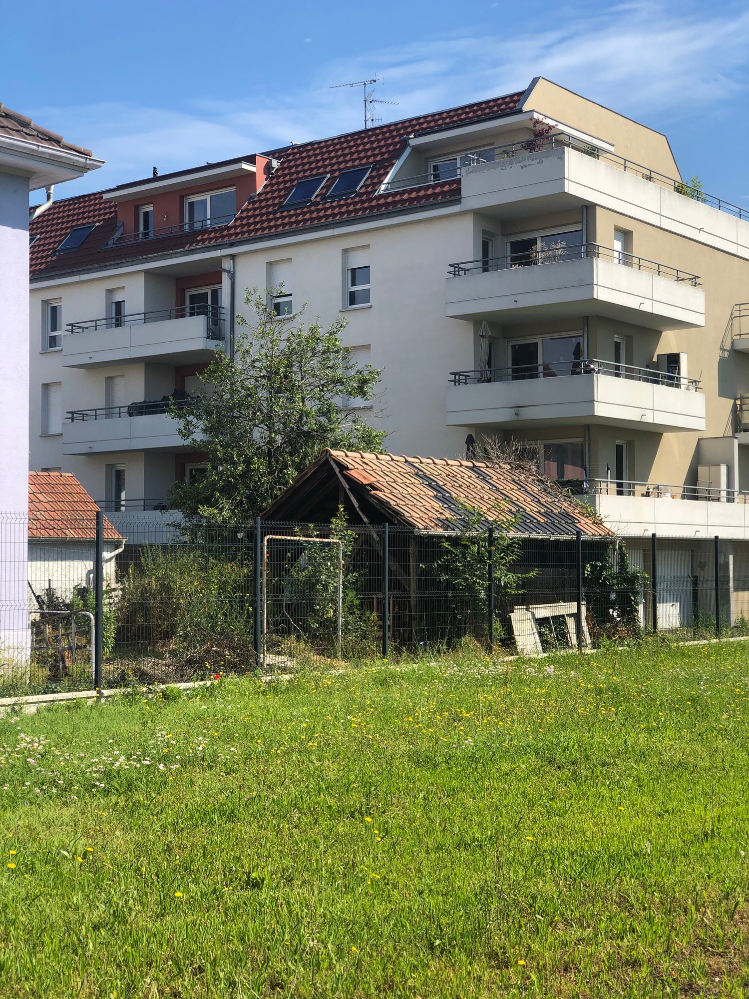 Multi-storey residential building, balconies on upper floors, fenced backyard with green grass