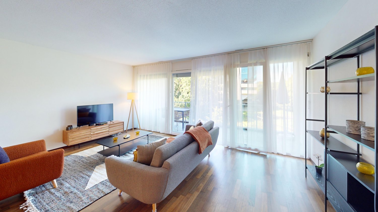 modern living room with hardwood floors, large windows, gray sofa, coffee table, TV, and decorative rug
