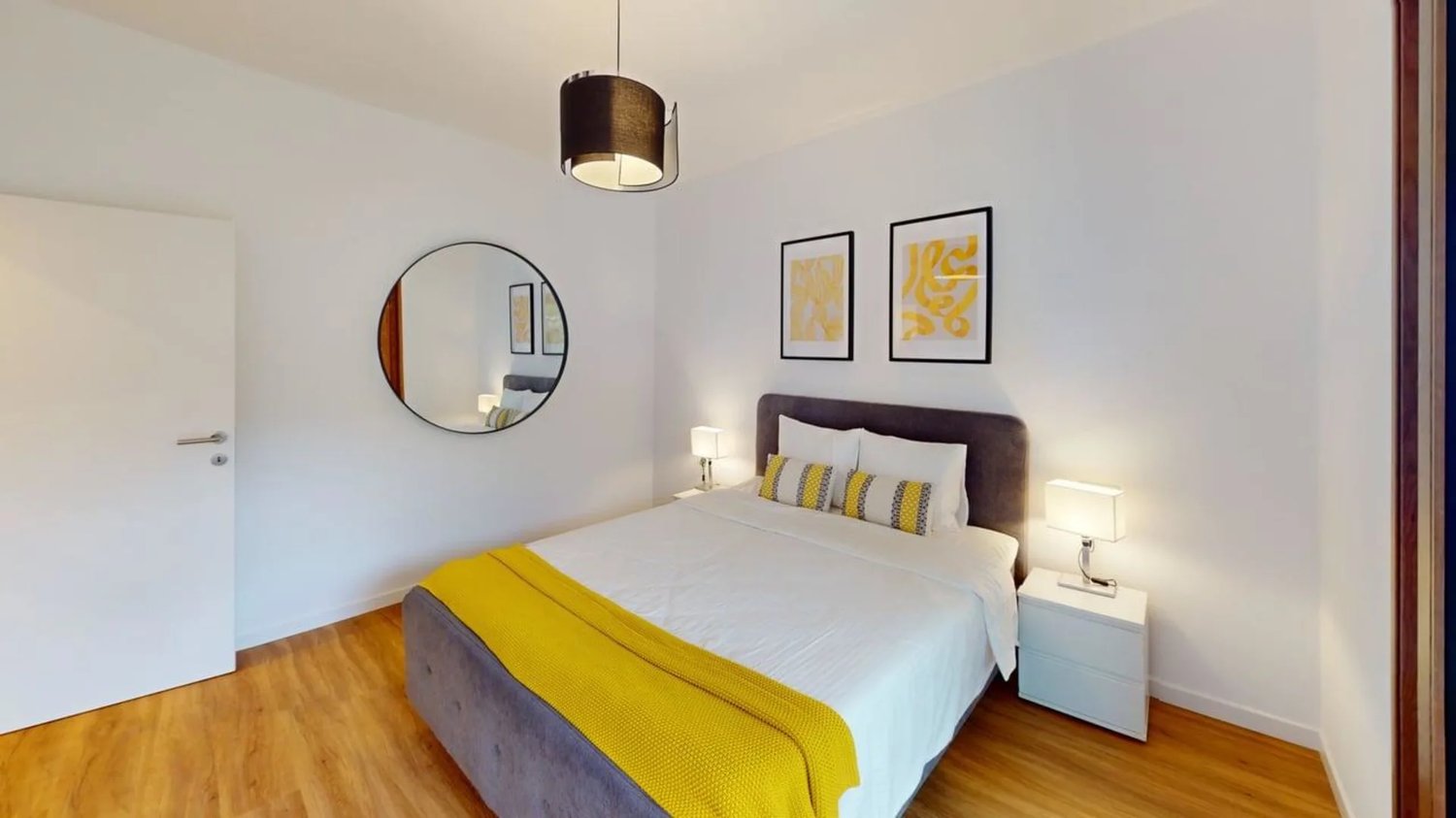 Queen-size bed, wooden floor, white walls, nightstands, lamps, circular mirror, framed pictures