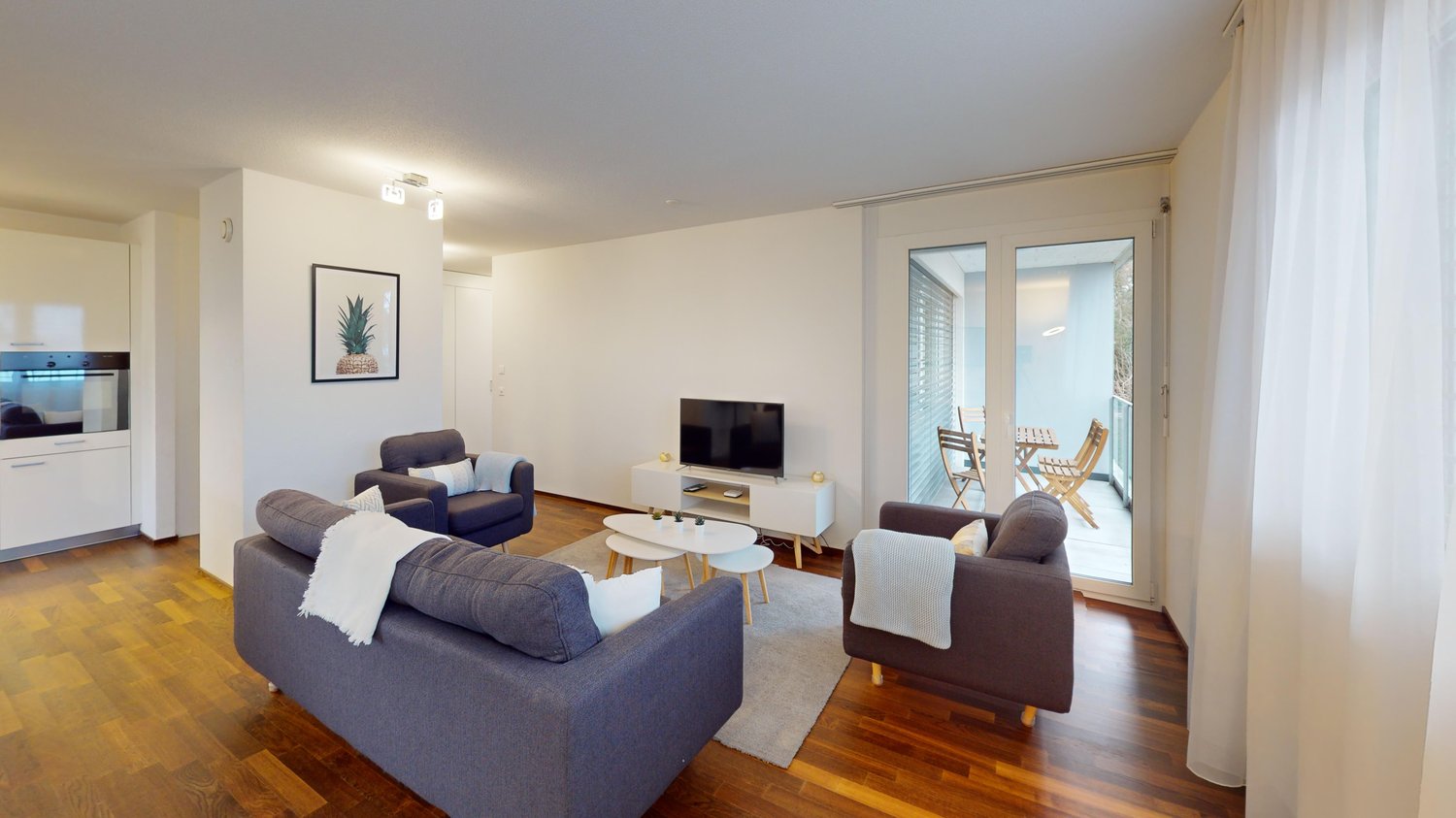 Spacious living room with hardwood floors, white walls, large windows, gray sofa set, coffee table, TV stand, and access to a balcony or terrace