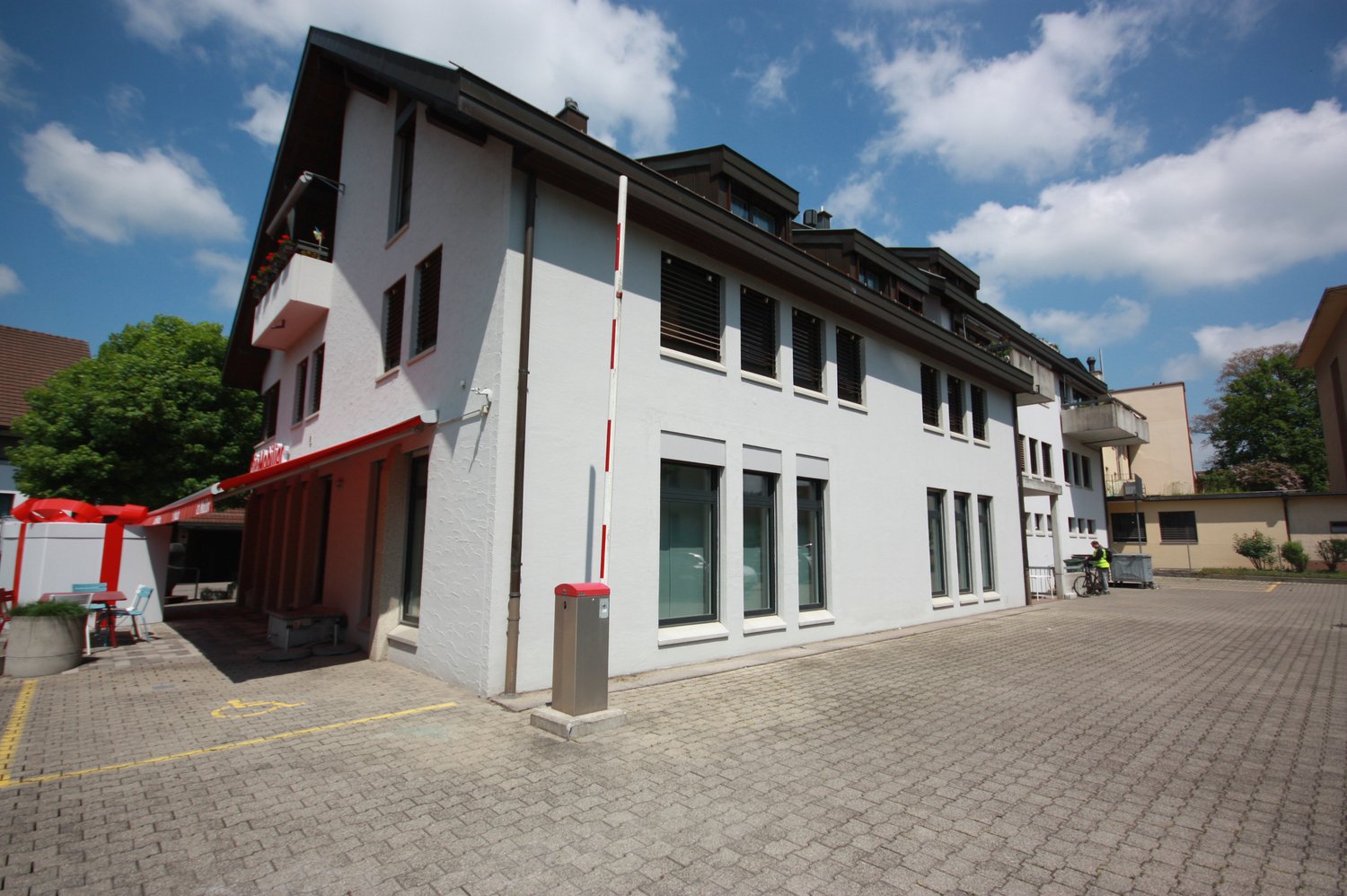 two-story house with a red awning over the entrance, several windows, a parking area in front