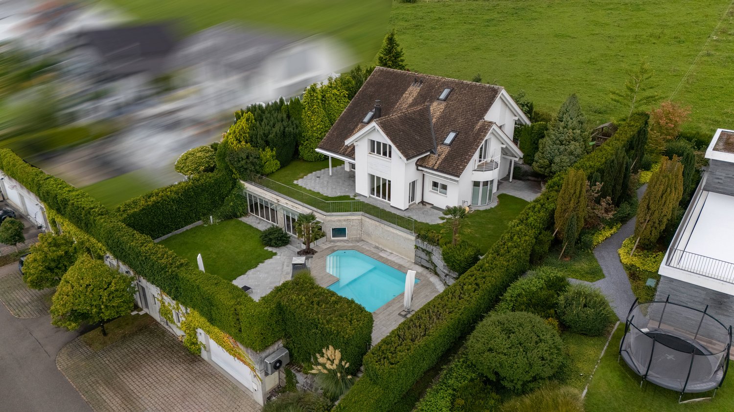 Two-story house, brown roof, white walls, pool in the garden, garden with hedges