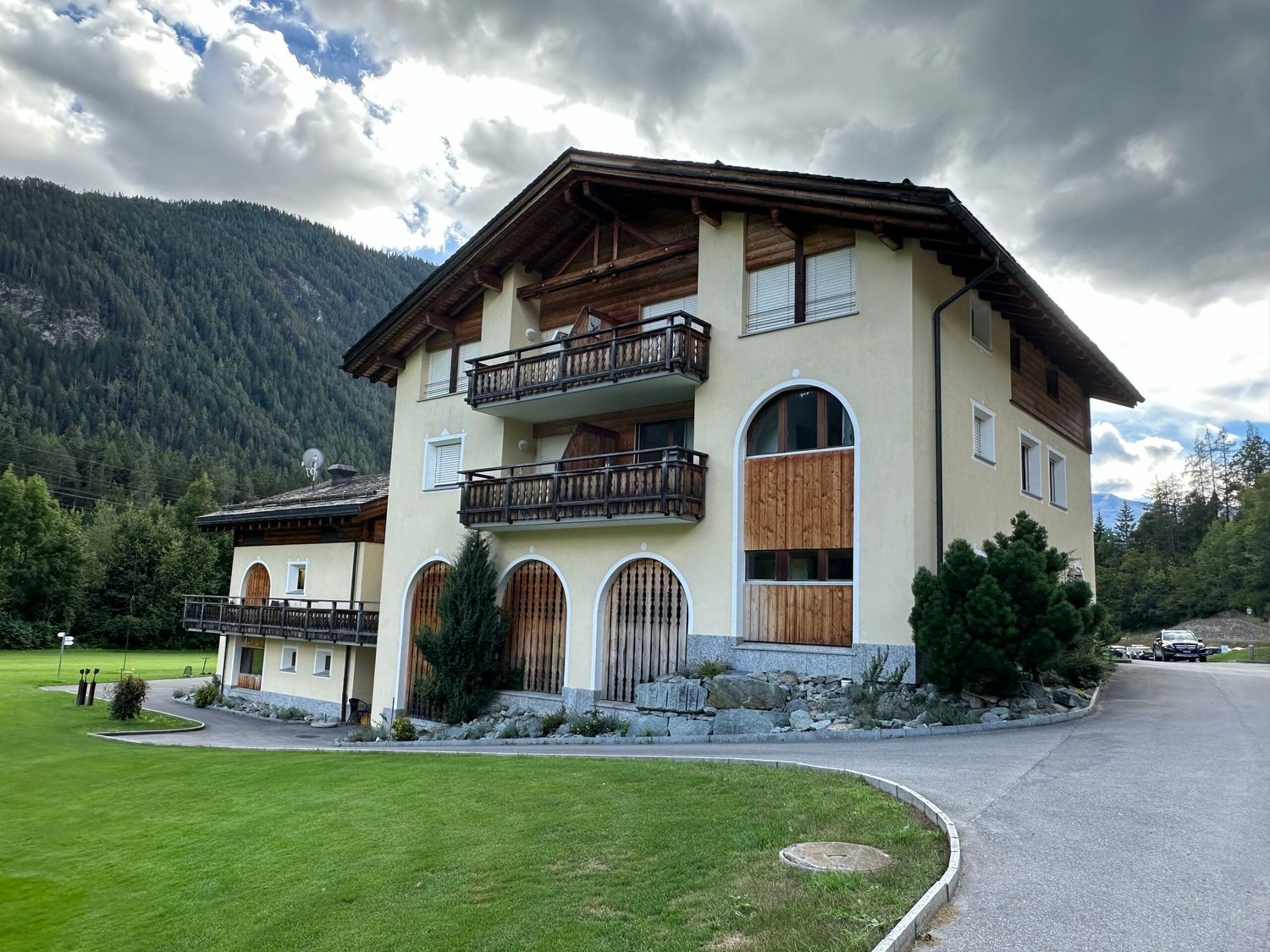 two story building, balconies, large grassy field, trees, mountains