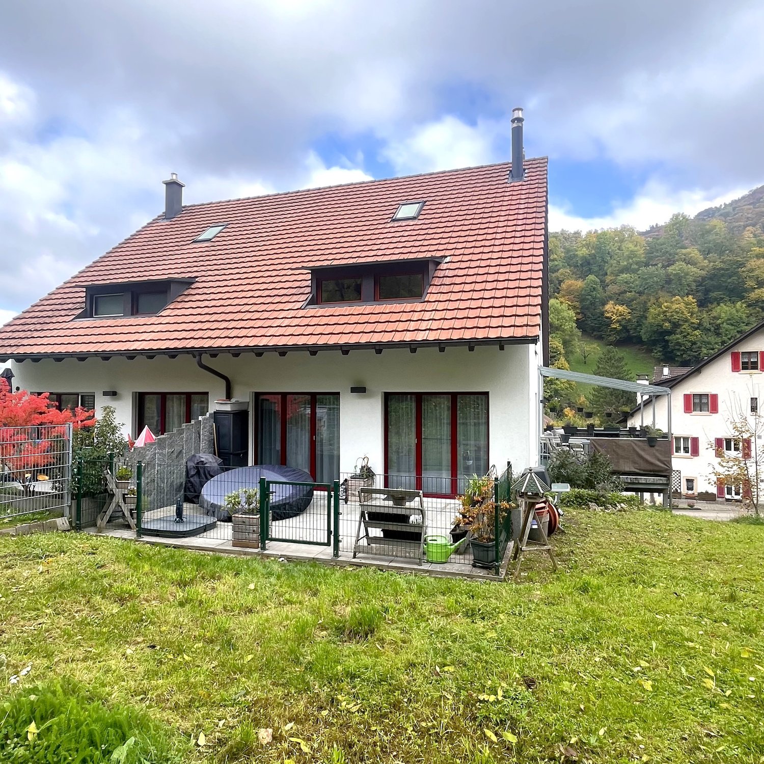 detached house, red roof, white walls, two stories, multiple windows, fenced yard, patio area, covered seating, garden with plants