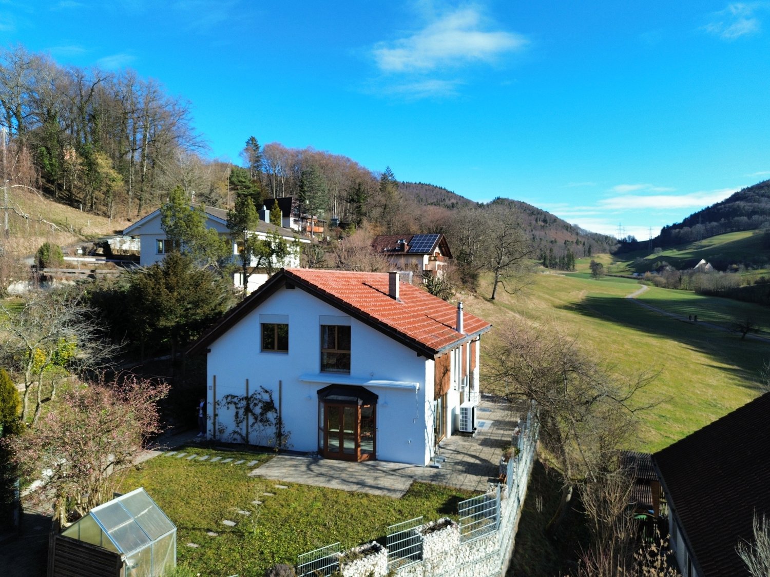 White house with red roof, raised ground floor, solar panels, spacious garden, surrounding green hills, good view