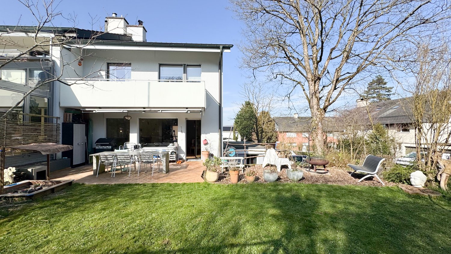 2 story house, white exterior, large windows, balcony, outdoor dining area, garden, trees, lawn