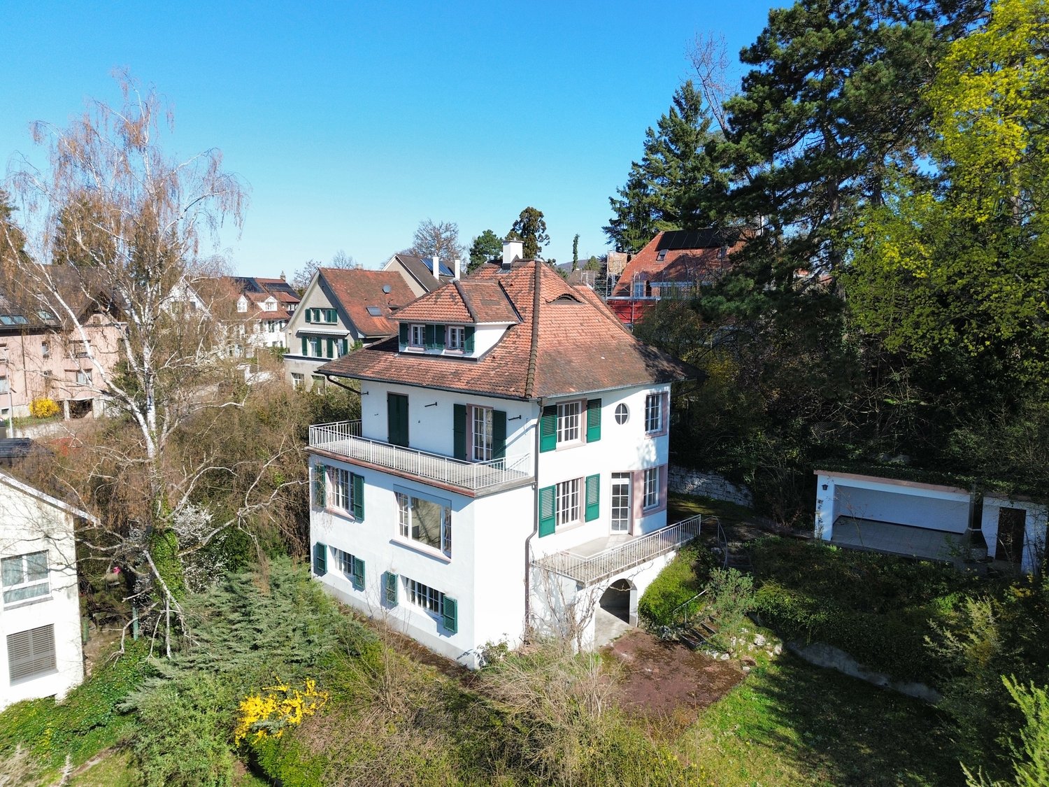 3 story house, white exterior, brown roof, green shutters, balcony, surrounded by trees