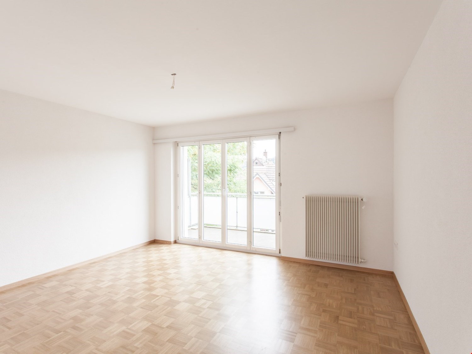 large room with white walls, wooden floor, sliding glass doors leading to a balcony, white radiator