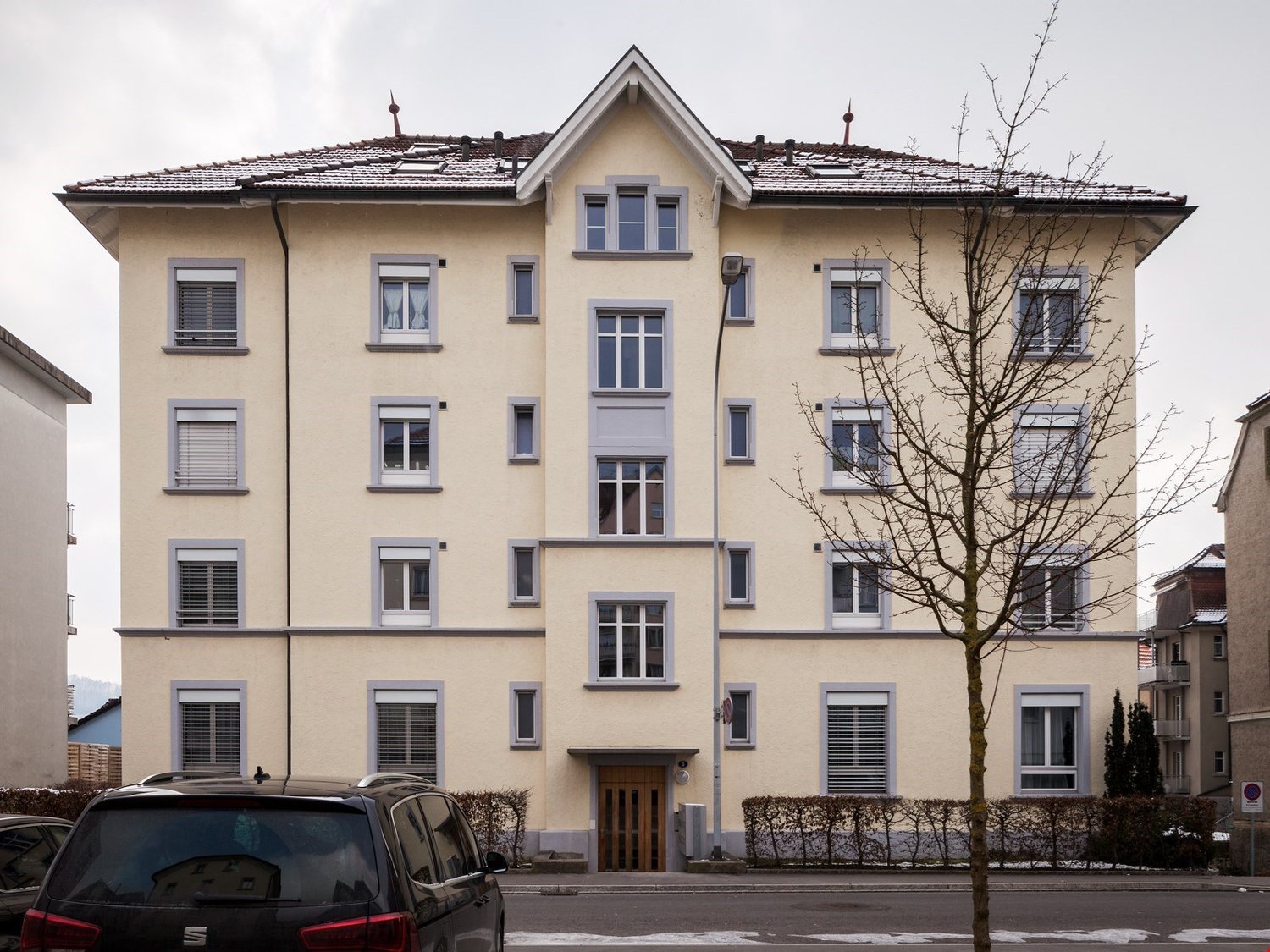 4 story building, beige walls, white windows, brown door, car parked in front