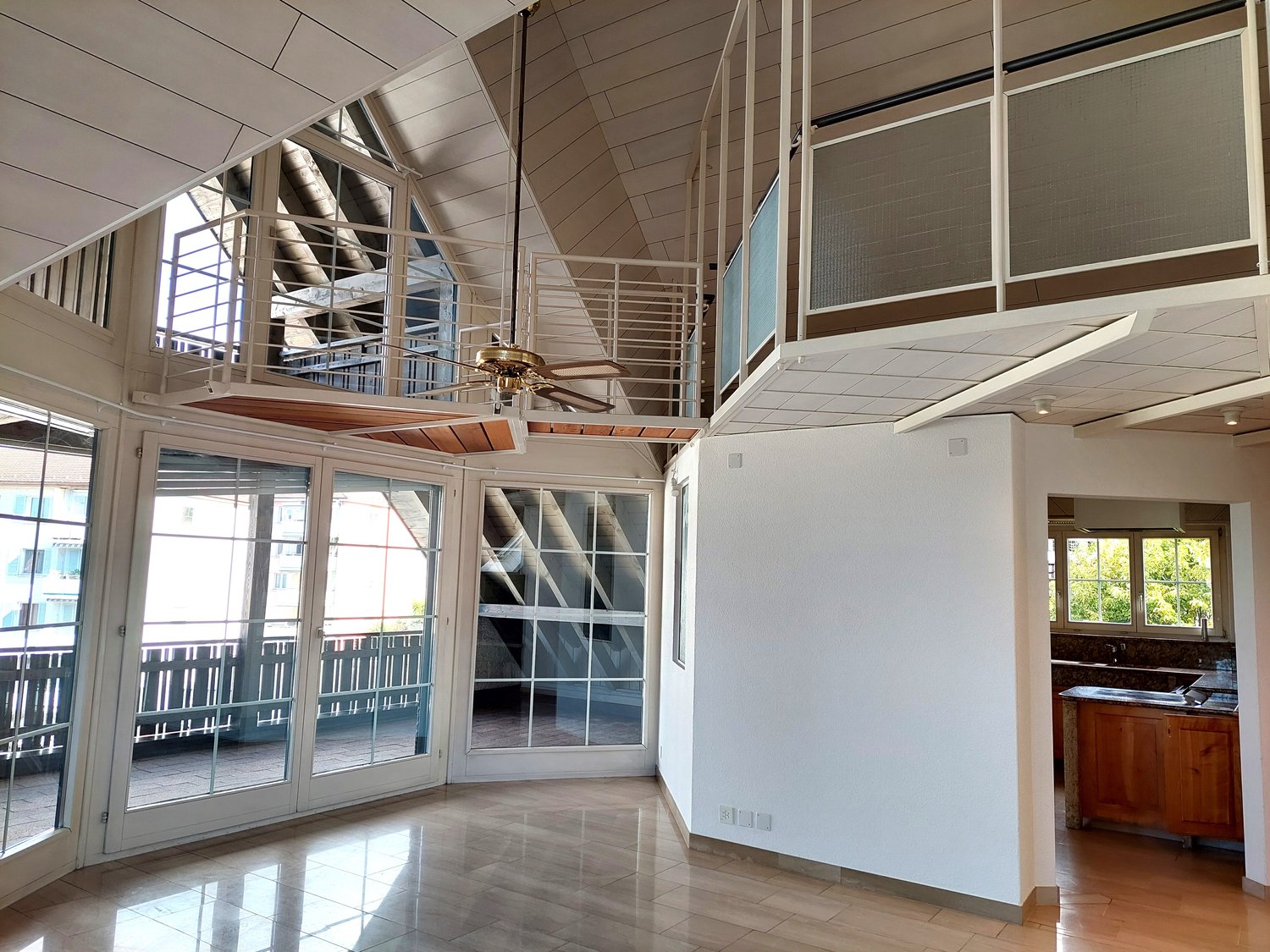 empty room, tiled floor, large windows, balcony with railing, ceiling fan, white walls, upper level with mezzanine and glass railings