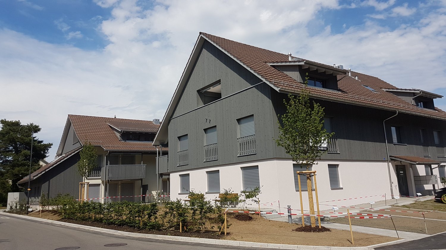 2 story house, gray exterior, brown roof, balcony, garden, white windows, fence around the garden, street light
