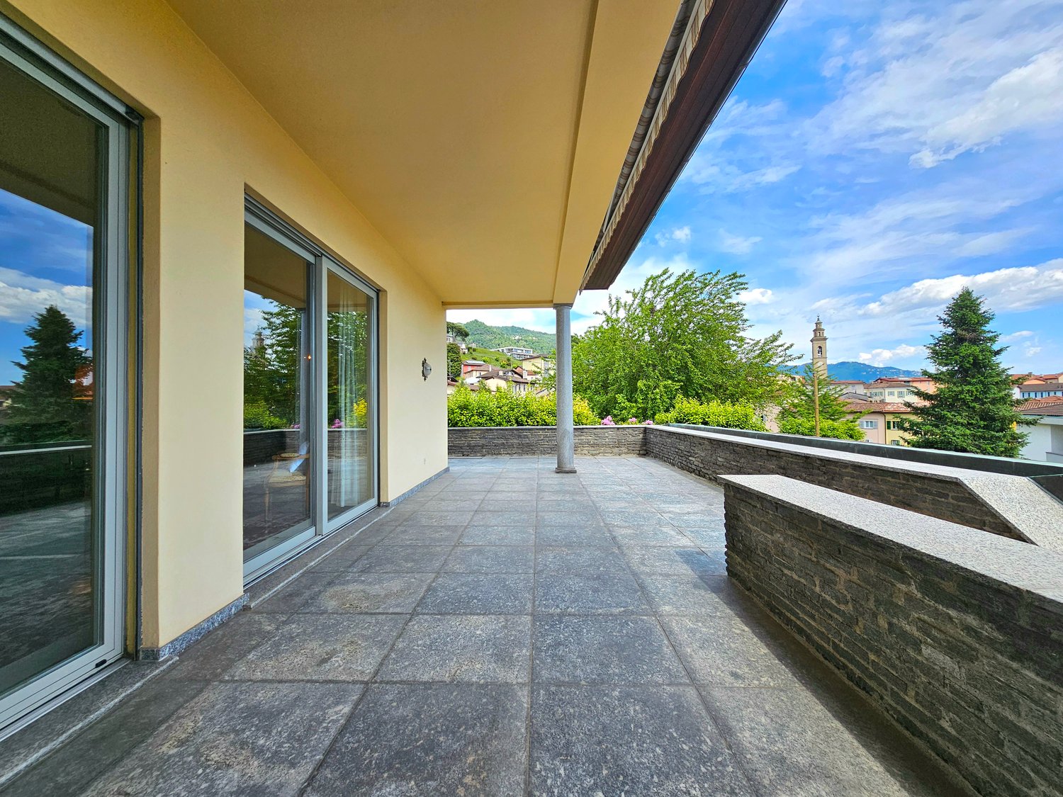 outdoor terrace with sliding glass doors, stone floor, stone railing, overlooking distant landscape
