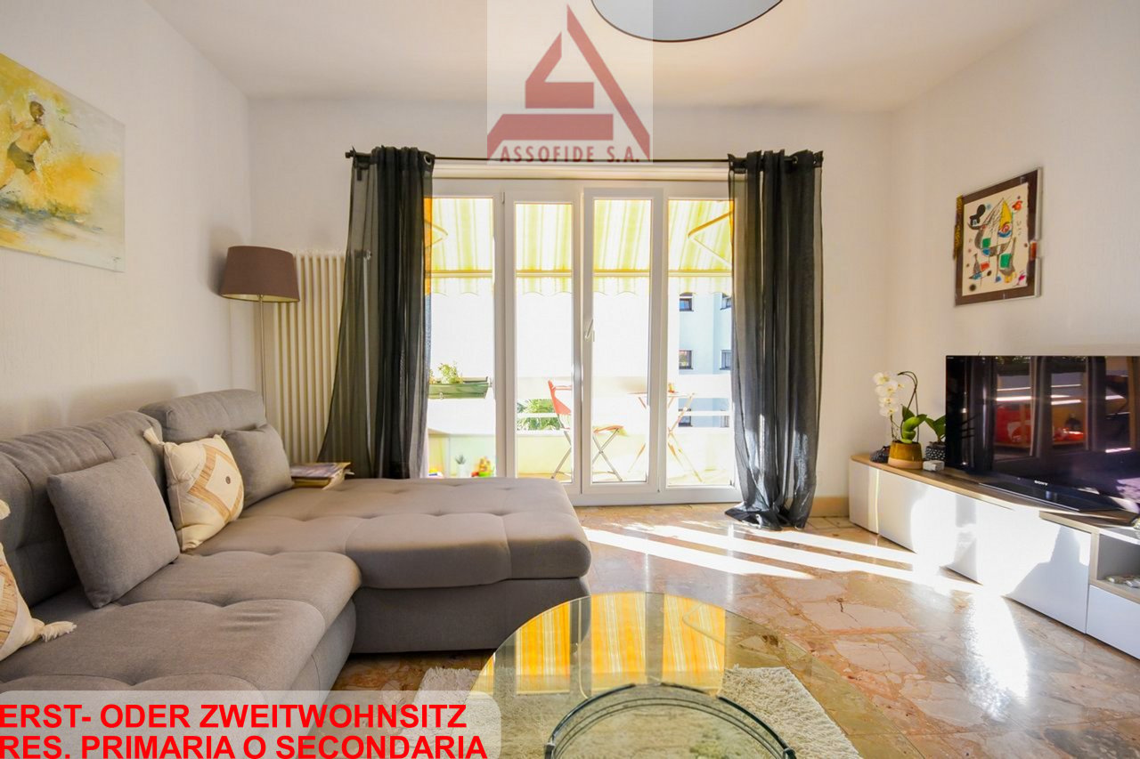 gray sofa, coffee table, floor lamp, artwork, sliding glass door to balcony, white tv stand, television, small potted plant
