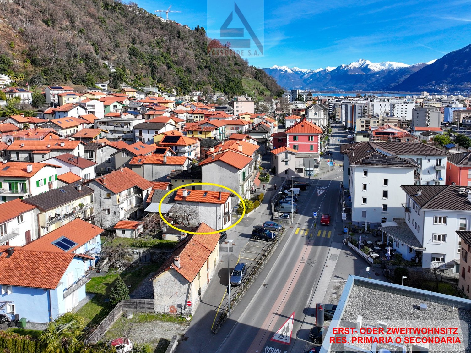 House in a village with red roofs, located on the side of the street, mountain view in the background.