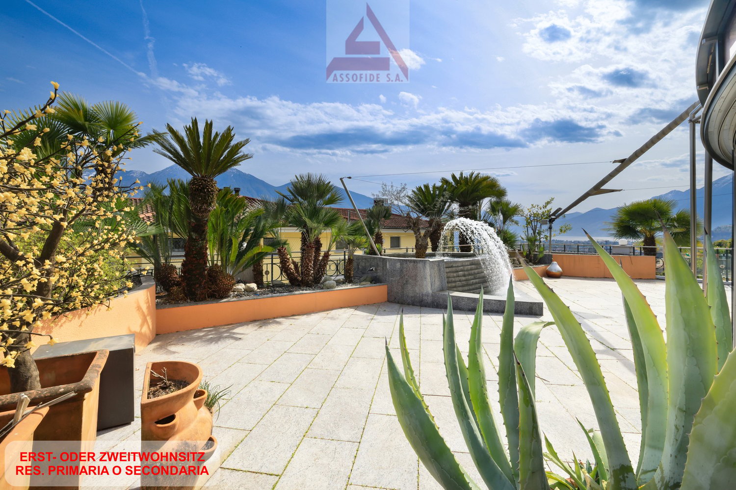 Outdoor area with fountain, tiled floor, various plants, and a view of mountains